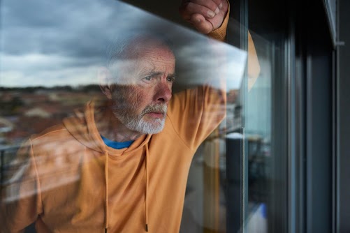 Worried older man looking out window, reflecting on another invoice payment